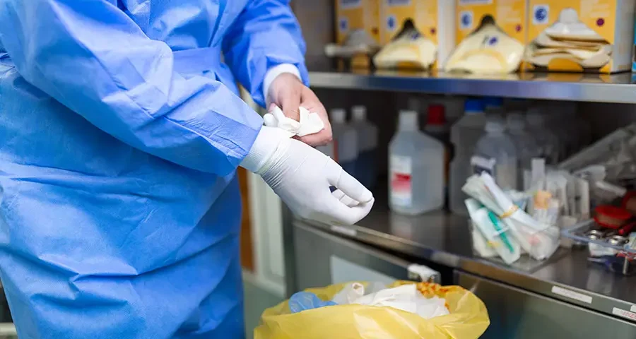 Male surgeon removing surgical gloves in a hospital operating room after a procedure.