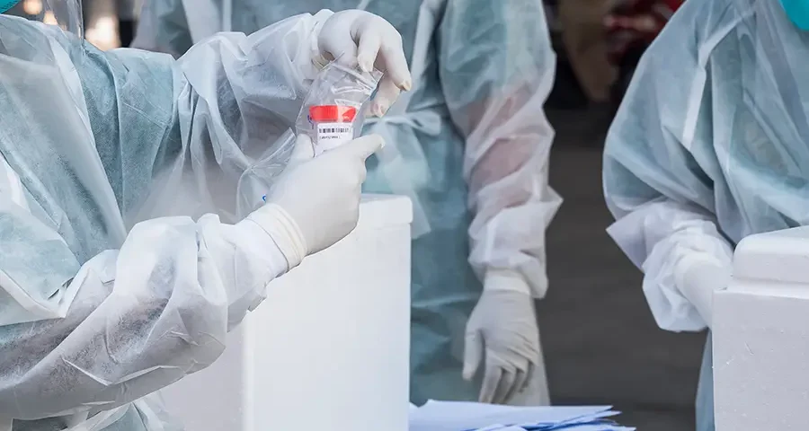Group of health workers collecting saliva samples for medical testing in a public outdoor area.