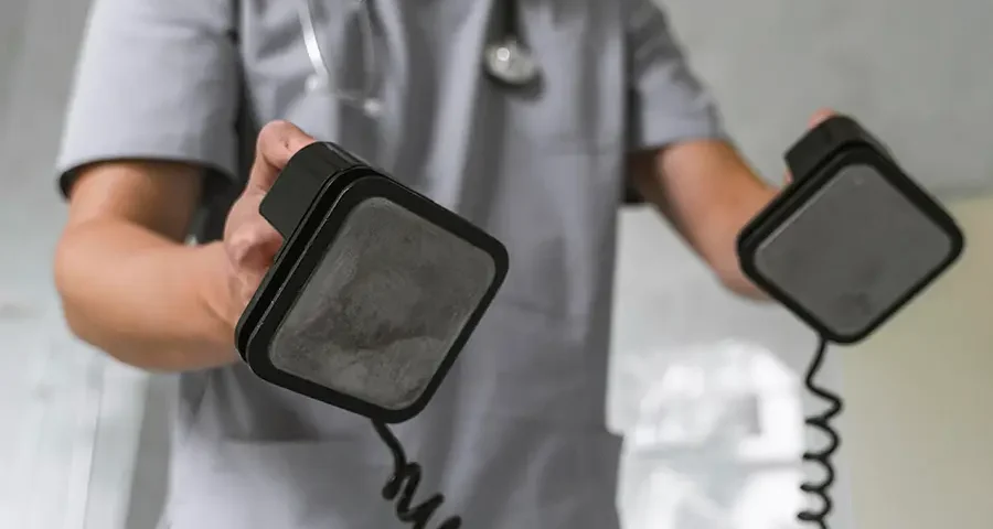 Doctor wearing a medical mask and stethoscope using a defibrillator in a clinical setting.