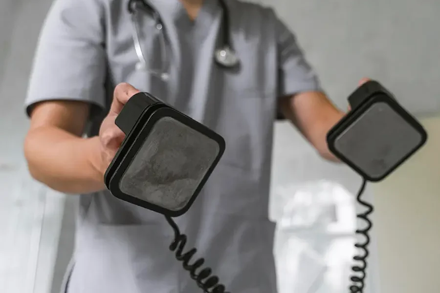 Doctor wearing a medical mask and stethoscope using a defibrillator in a clinical setting.