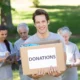 Smiling volunteer holding a donation box filled with medical and healthcare supplies.