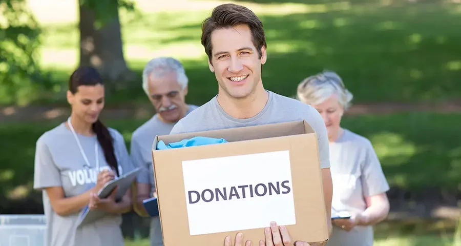 Smiling volunteer holding a donation box filled with medical and healthcare supplies.