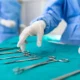 Nurse picking up a surgical instrument in an operating room, with surgeons working in the background.