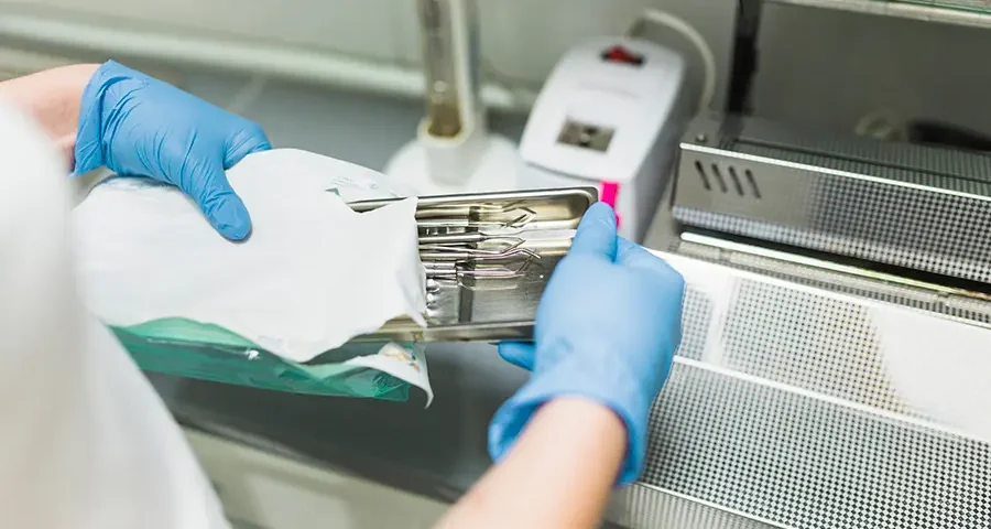 Nurse hand packing sterilized dental instruments into plastic bags in a healthcare facility.