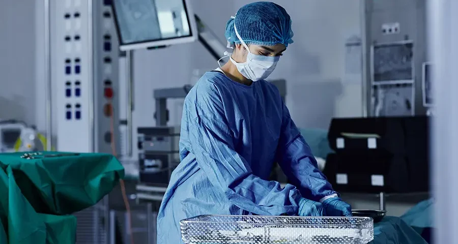 Female doctor preparing surgical equipment in a hospital operating room with proper PPE.