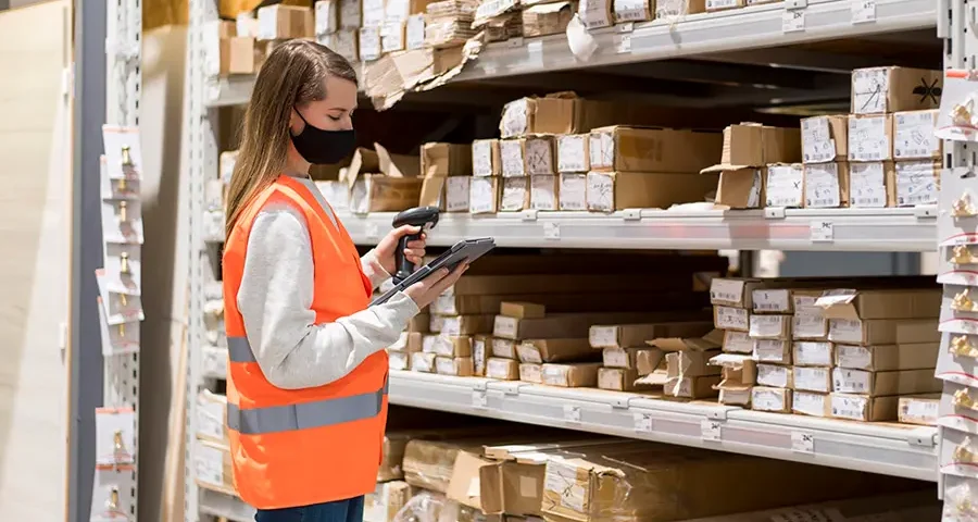 Woman wearing a face mask and standing in a warehouse filled with medical supplies.