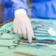 Surgeon selecting a surgical tool from a tray while preparing for surgery in a hospital operating room.
