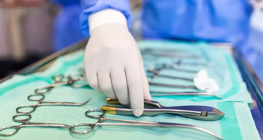 Surgeon selecting a surgical tool from a tray while preparing for surgery in a hospital operating room.