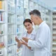 Smiling pharmacist with a colleague holding medicine bottles in a pharmacy.
