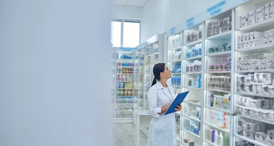 Pharmacist reviewing and organizing medicines on pharmacy shelves.