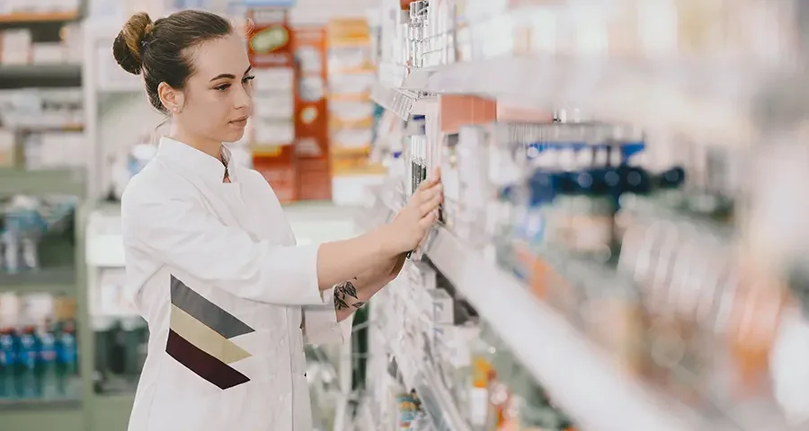 Female pharmacist retrieving medications from a shelf in a modern pharmacy.
