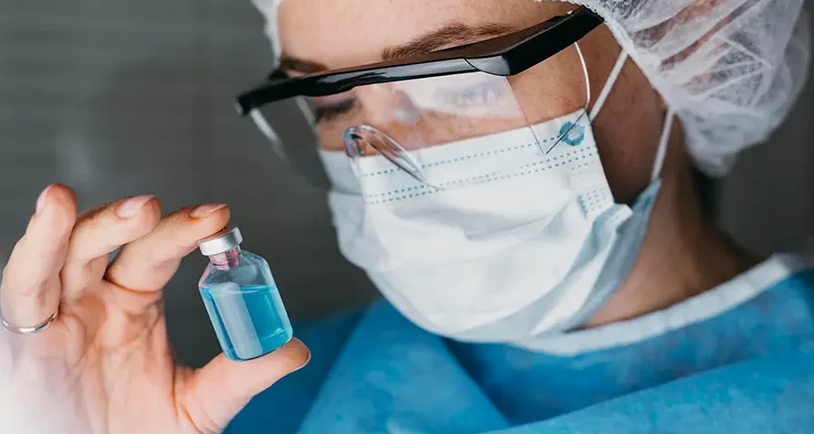 Doctor wearing gloves holding a vaccine vial in focus.