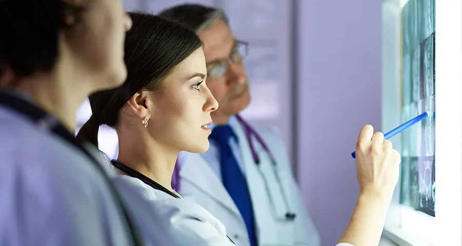 Group of doctors analyzing X-ray films together in a clinical setting, discussing possible diagnoses.
