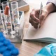 Close-up of a scientist’s hand taking notes during a research session, surrounded by lab equipment.