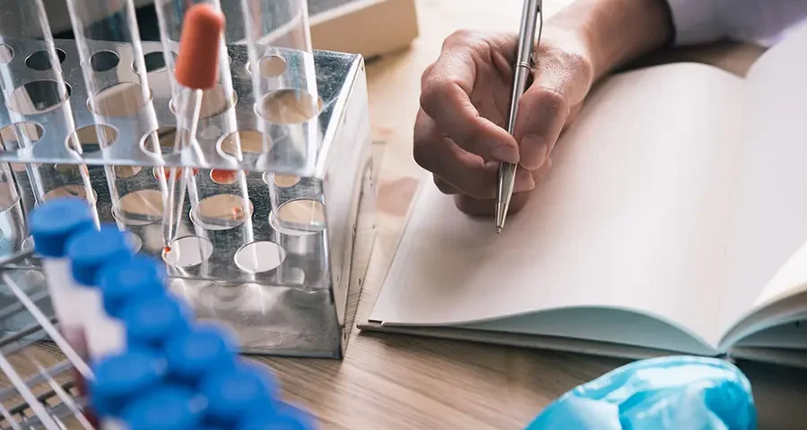 Close-up of a scientist’s hand taking notes during a research session, surrounded by lab equipment.