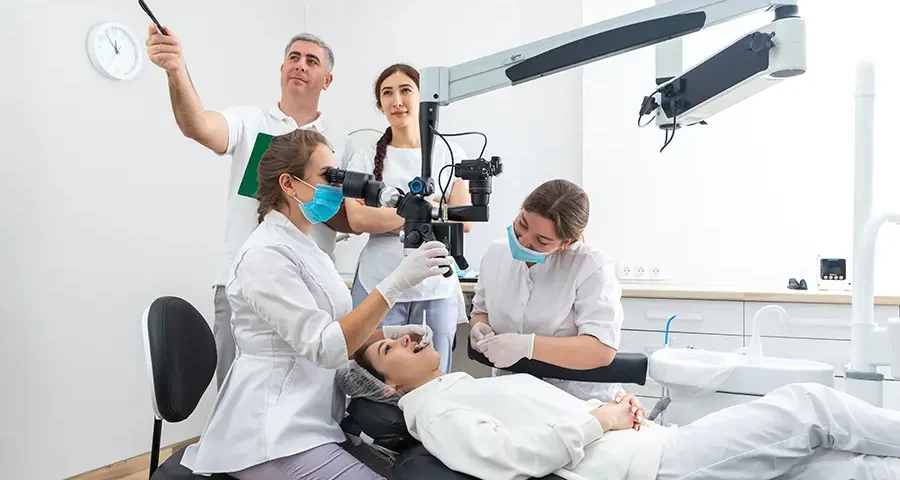 Dental students observing treatment through a microscope during clinical training.