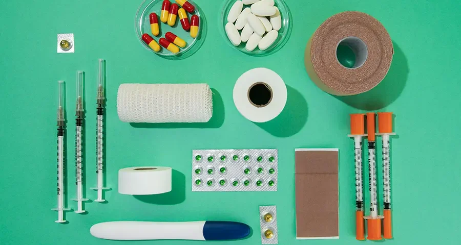 Various medical supplies such as syringes, gauze, adhesive tapes, and pills arranged neatly on a green background.