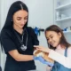 Veterinarian in black scrubs with a stethoscope examining a guinea pig while a smiling young girl watches at a veterinary clinic.